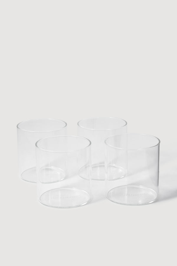 Four clear cylindrical tumbler glasses arranged in a loose square on a white studio background.