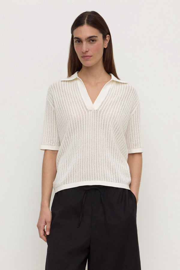 A woman wearing a short sleeve ribbed knit polo shirt in antique white, paired with black drawstring pants, against a plain white background.